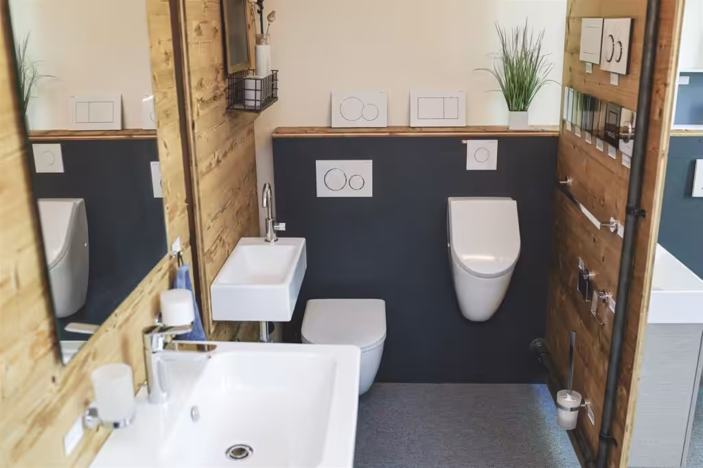 Waschtisch, Wand-WC und Urinal vor Anthrazitwand und Altholz in der Ausstellung
