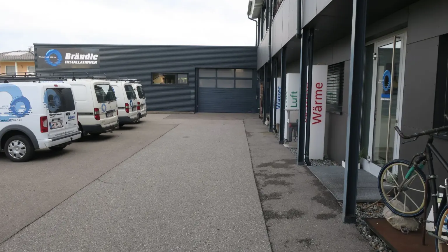 Hof des Betriebsgebäudes in Altach mit Firmenfahrzeugen und den Säulen Wasser, Luft, Wärme